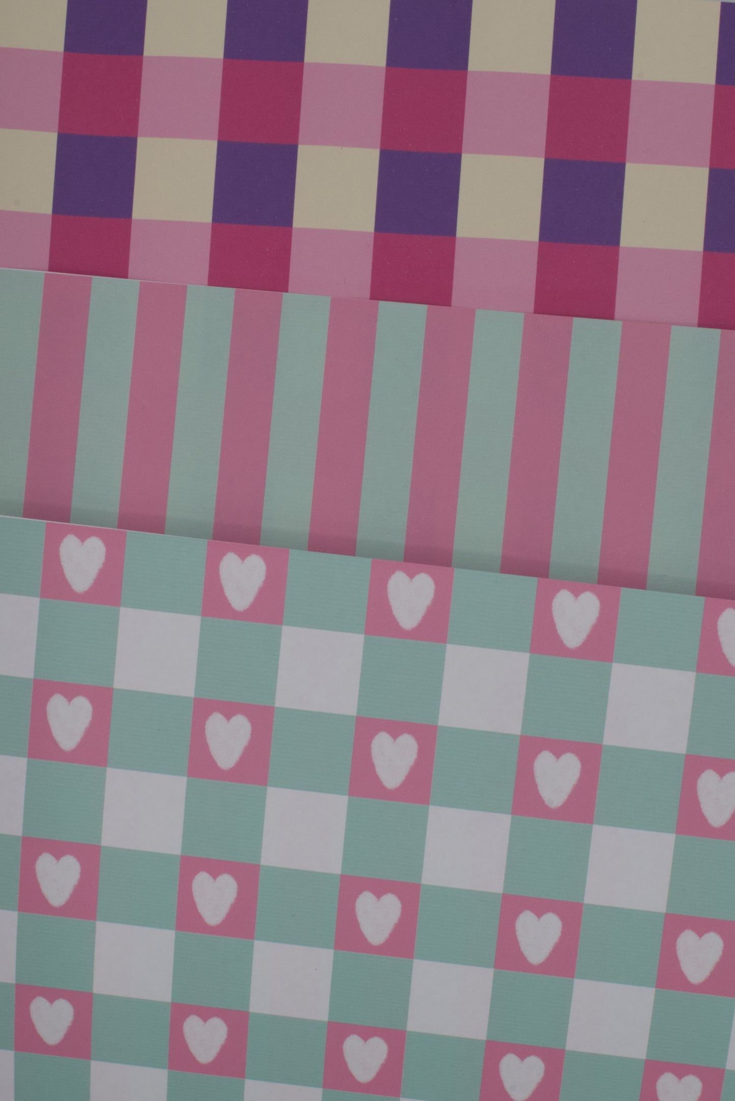 Checkered fabric with pink and purple squares and white hearts on a green and pink checkered background.