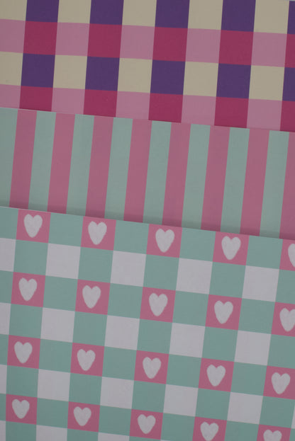 Checkered fabric with pink and purple squares and white hearts on a green and pink checkered background.